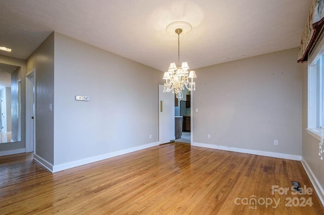 unfurnished room featuring an inviting chandelier and light wood-type flooring