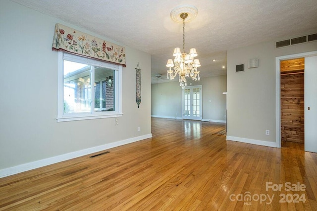 unfurnished dining area with a textured ceiling, hardwood / wood-style flooring, and an inviting chandelier