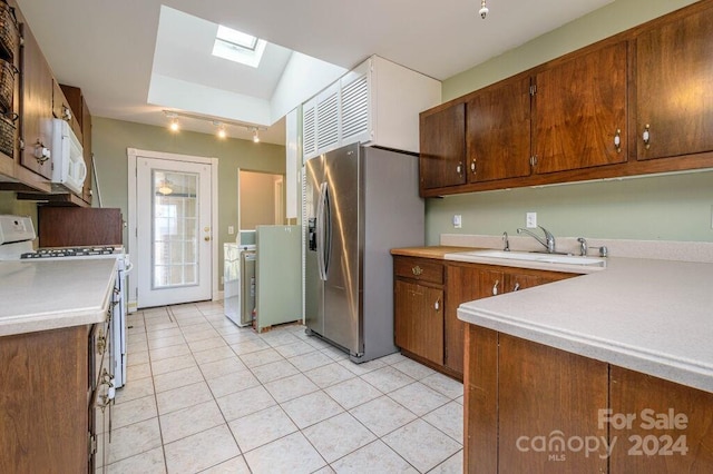 kitchen with sink, rail lighting, lofted ceiling with skylight, white appliances, and light tile patterned floors