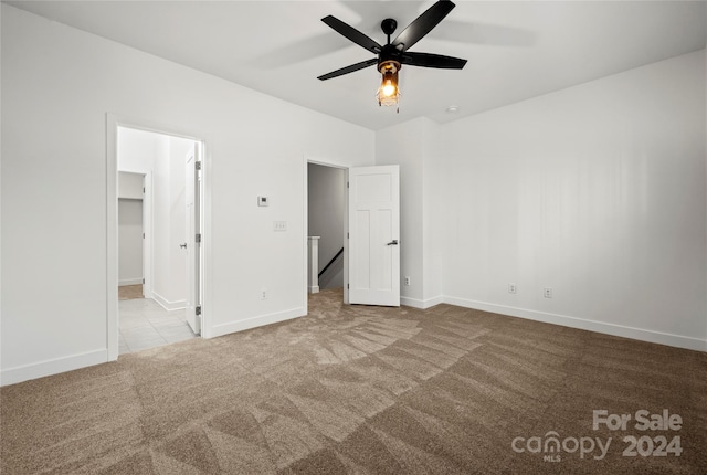 unfurnished bedroom featuring light carpet, a closet, a spacious closet, and ceiling fan