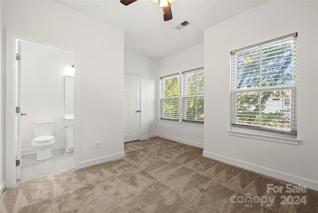 unfurnished bedroom featuring ceiling fan, light carpet, and ensuite bath