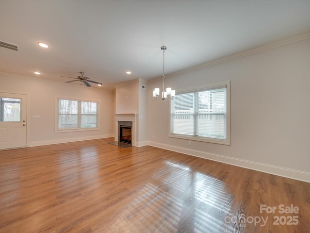 unfurnished living room with ceiling fan with notable chandelier, a healthy amount of sunlight, and crown molding