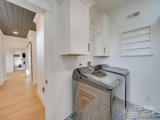 clothes washing area with washing machine and clothes dryer, cabinets, a barn door, light hardwood / wood-style floors, and wood ceiling