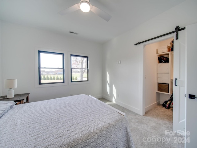 carpeted bedroom featuring ceiling fan, a barn door, and a spacious closet