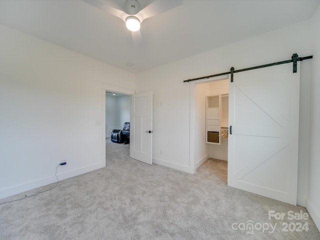 unfurnished bedroom with ceiling fan, a barn door, and light carpet