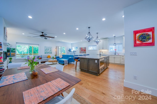 dining room featuring ceiling fan with notable chandelier, sink, a wealth of natural light, and light hardwood / wood-style flooring