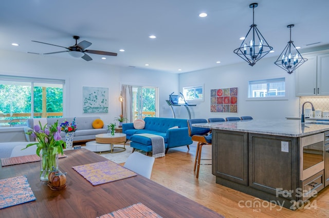 living room with light hardwood / wood-style flooring, ceiling fan with notable chandelier, and sink