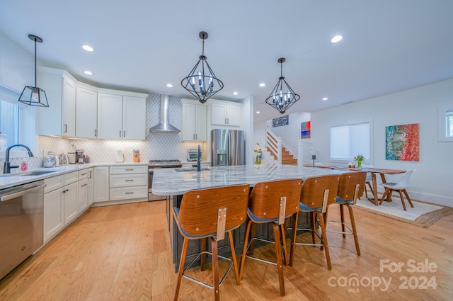 kitchen featuring appliances with stainless steel finishes, wall chimney exhaust hood, sink, white cabinets, and a kitchen island