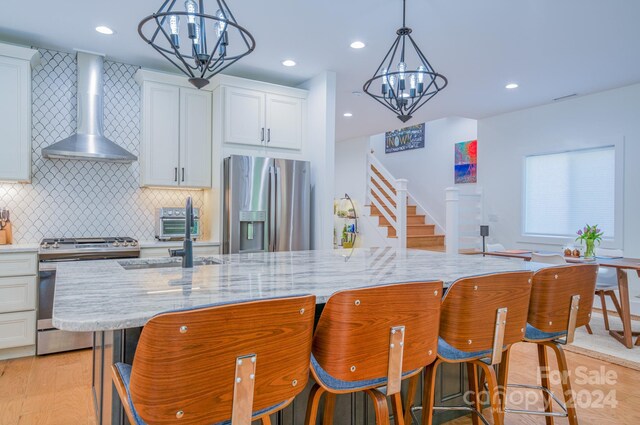 kitchen featuring wall chimney exhaust hood, light wood-type flooring, appliances with stainless steel finishes, a large island, and white cabinetry