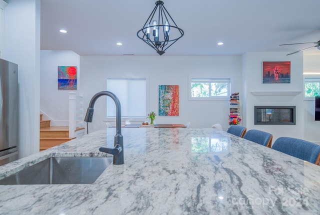 kitchen featuring stainless steel fridge, ceiling fan with notable chandelier, sink, hardwood / wood-style flooring, and decorative light fixtures