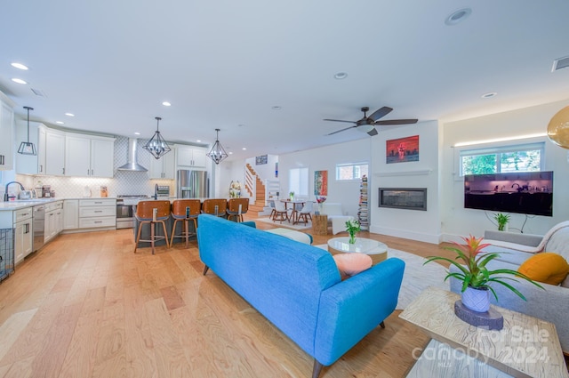 living room with ceiling fan with notable chandelier, light hardwood / wood-style floors, and sink