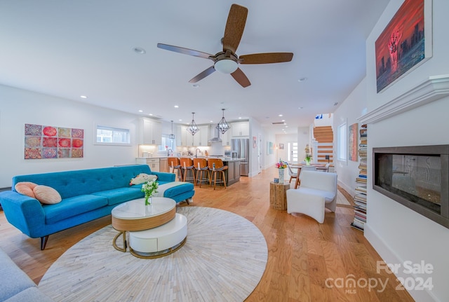 living room featuring ceiling fan with notable chandelier and light hardwood / wood-style floors