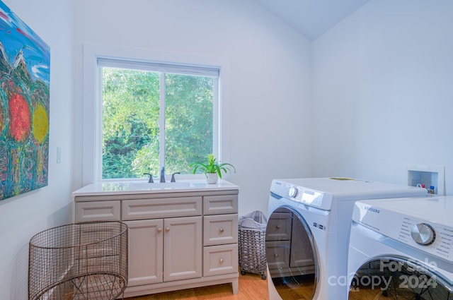 clothes washing area with washer and clothes dryer, light hardwood / wood-style floors, cabinets, and sink