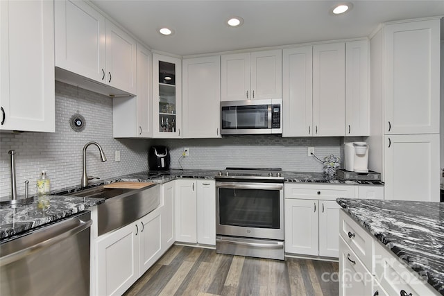 kitchen with stainless steel appliances, white cabinetry, tasteful backsplash, and dark stone counters