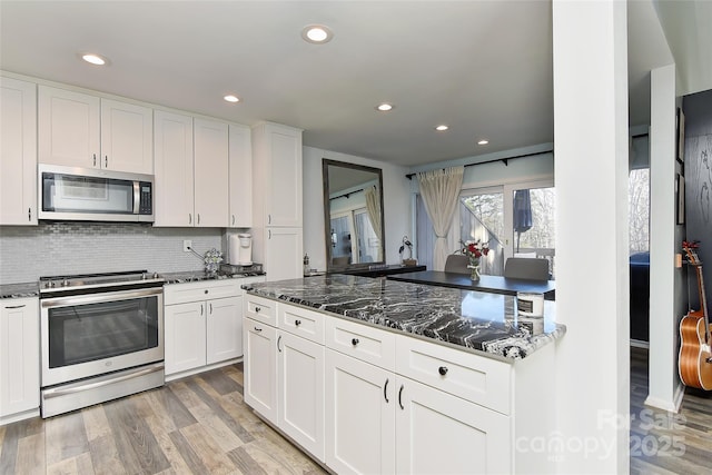 kitchen featuring appliances with stainless steel finishes, white cabinets, dark stone counters, light hardwood / wood-style floors, and backsplash