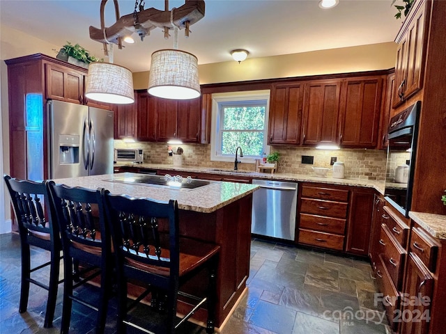 kitchen featuring sink, backsplash, pendant lighting, a kitchen island, and appliances with stainless steel finishes