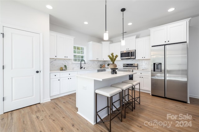 kitchen featuring light wood-type flooring, stainless steel appliances, white cabinetry, and hanging light fixtures