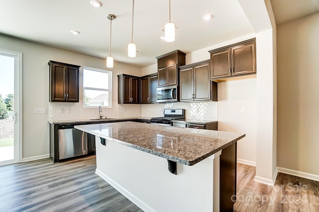 kitchen featuring pendant lighting, dark stone counters, light hardwood / wood-style floors, appliances with stainless steel finishes, and a kitchen island