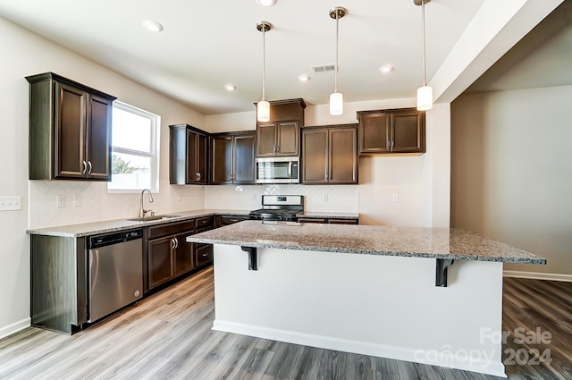 kitchen with light stone counters, stainless steel appliances, sink, pendant lighting, and a center island