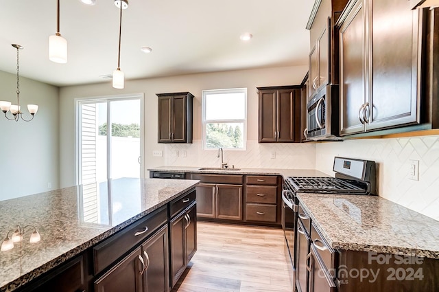 kitchen with sink, hanging light fixtures, light hardwood / wood-style flooring, light stone counters, and stainless steel appliances