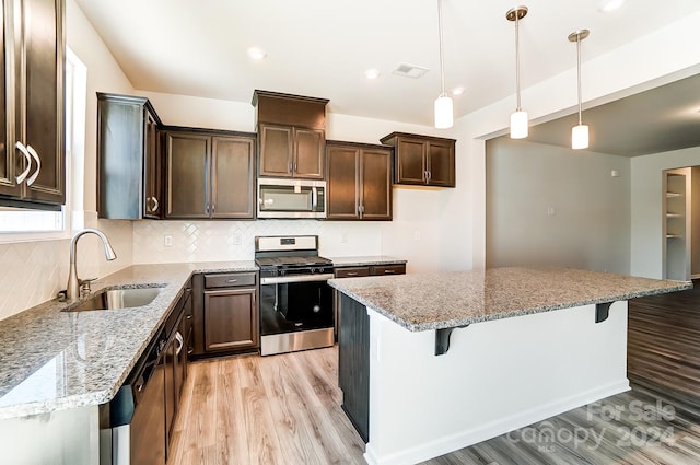 kitchen featuring light stone countertops, a kitchen island, light wood-type flooring, and appliances with stainless steel finishes