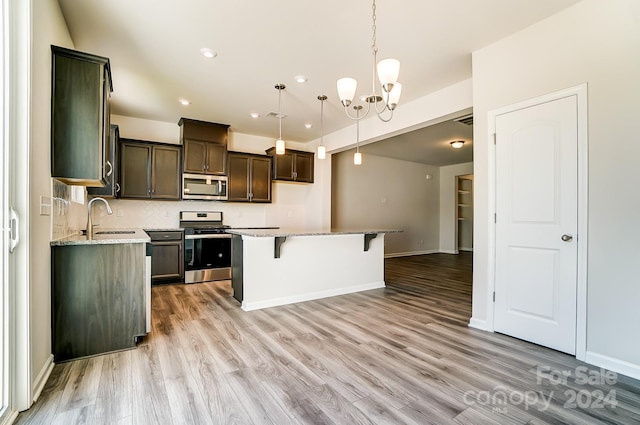 kitchen with sink, light stone counters, light hardwood / wood-style flooring, a kitchen island, and appliances with stainless steel finishes