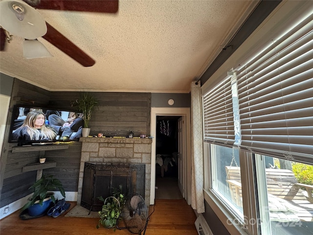 living room with crown molding, wood walls, wood-type flooring, a textured ceiling, and a fireplace