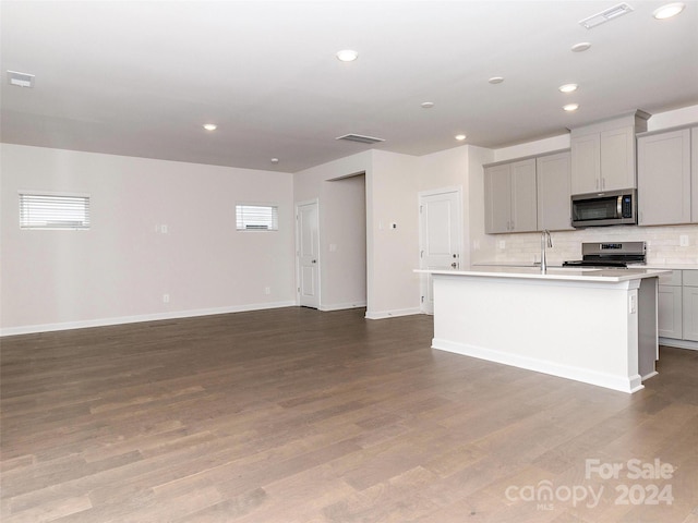 kitchen with appliances with stainless steel finishes, gray cabinets, and an island with sink