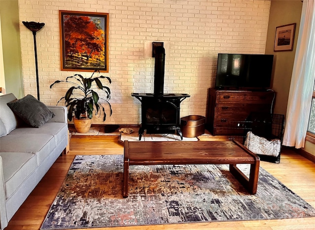 living room with hardwood / wood-style floors, a wood stove, and brick wall