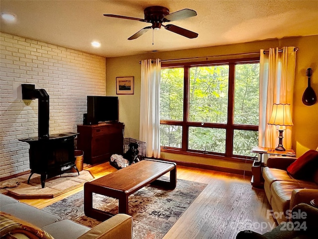 living room with brick wall, a textured ceiling, ceiling fan, light hardwood / wood-style flooring, and a wood stove