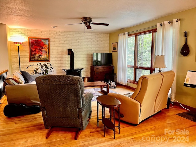 living room with ceiling fan, light wood-type flooring, a textured ceiling, and a wood stove