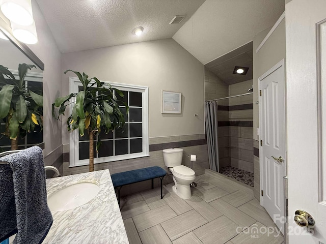 bathroom with a textured ceiling, tile walls, toilet, walk in shower, and vanity