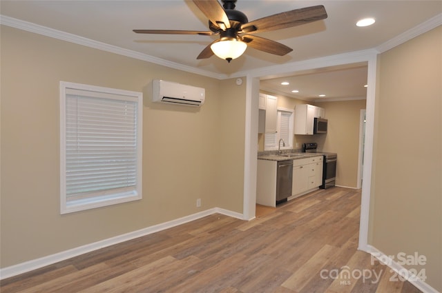 kitchen with appliances with stainless steel finishes, light wood-type flooring, a wall unit AC, crown molding, and white cabinets