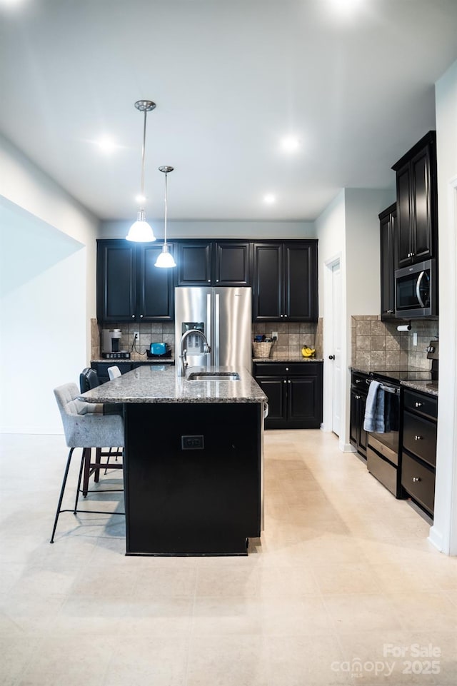 kitchen with pendant lighting, sink, an island with sink, light stone counters, and stainless steel appliances