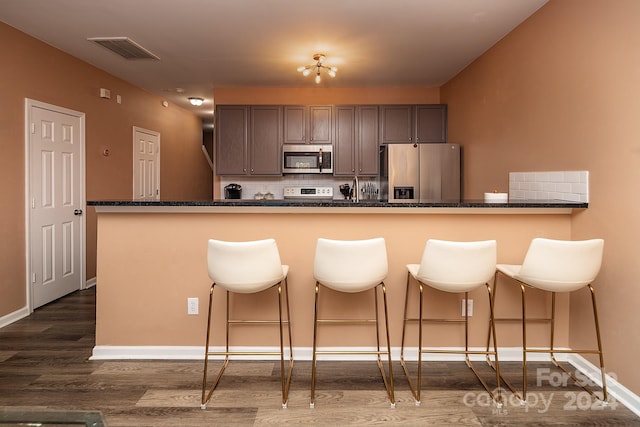 kitchen with kitchen peninsula, decorative backsplash, dark hardwood / wood-style flooring, stainless steel appliances, and a breakfast bar area