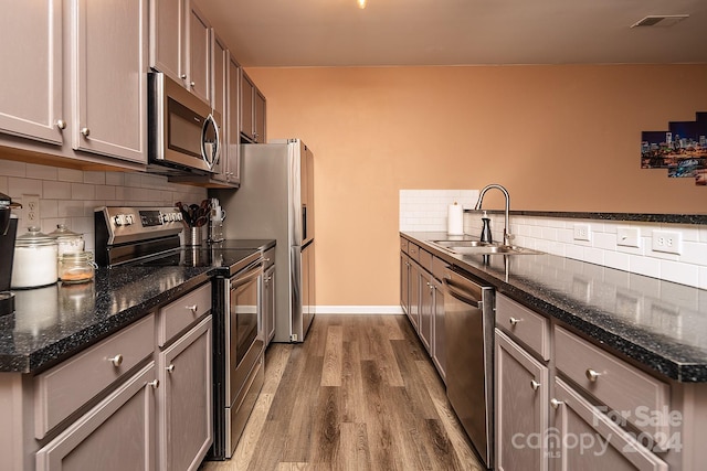 kitchen featuring wood-type flooring, sink, stainless steel appliances, and dark stone countertops