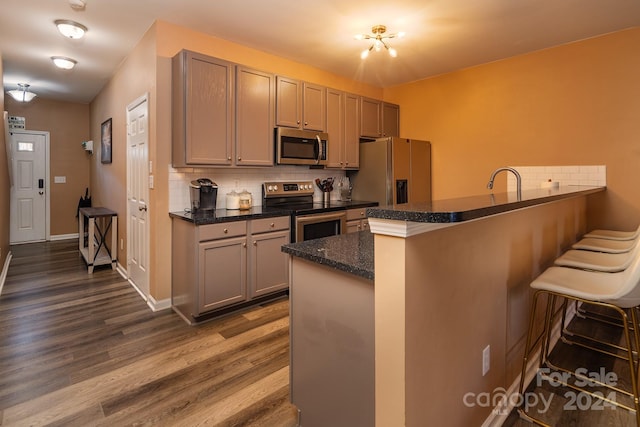 kitchen with tasteful backsplash, kitchen peninsula, hardwood / wood-style floors, a breakfast bar, and appliances with stainless steel finishes