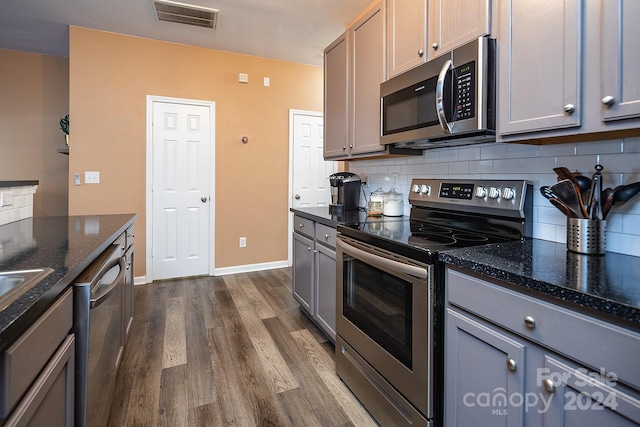 kitchen featuring dark stone counters, dark hardwood / wood-style floors, gray cabinets, appliances with stainless steel finishes, and tasteful backsplash