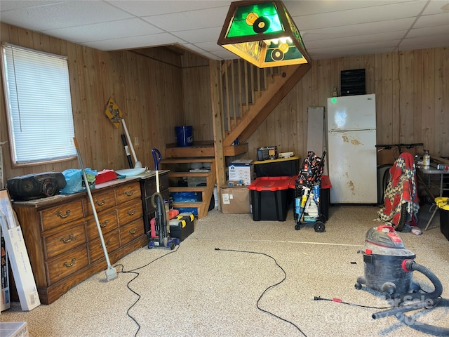 interior space with carpet flooring, white refrigerator, a drop ceiling, and wooden walls