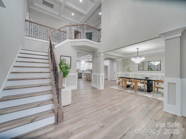 foyer entrance with beam ceiling, ornate columns, light hardwood / wood-style flooring, a notable chandelier, and a towering ceiling