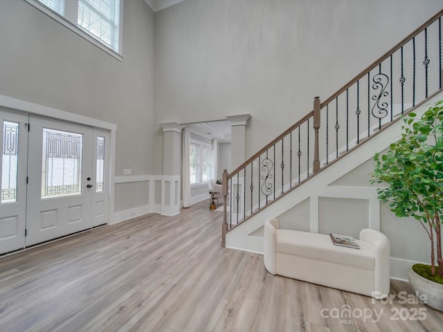 entrance foyer with light wood-type flooring, decorative columns, stairs, and a high ceiling