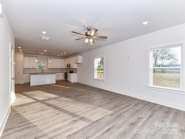 unfurnished living room featuring visible vents, a sink, recessed lighting, light wood finished floors, and baseboards