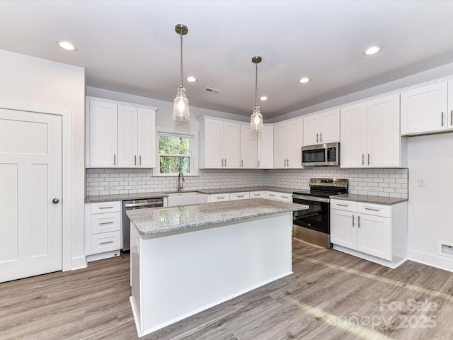 kitchen featuring a center island, appliances with stainless steel finishes, light wood-style floors, white cabinetry, and a sink