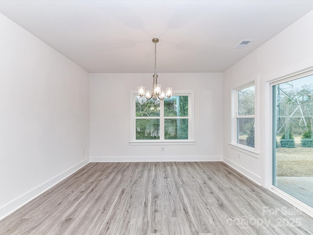 empty room featuring an inviting chandelier, light wood-style floors, visible vents, and baseboards