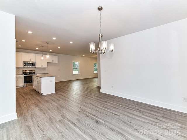 kitchen with stainless steel appliances, decorative backsplash, white cabinets, light wood-style floors, and open floor plan