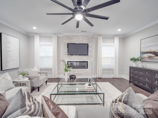 living room featuring hardwood / wood-style floors, a stone fireplace, ornamental molding, and a healthy amount of sunlight