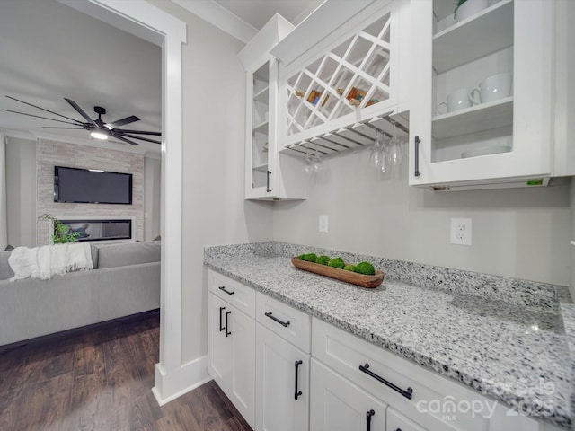 kitchen with white cabinets, ceiling fan, dark hardwood / wood-style floors, ornamental molding, and light stone counters