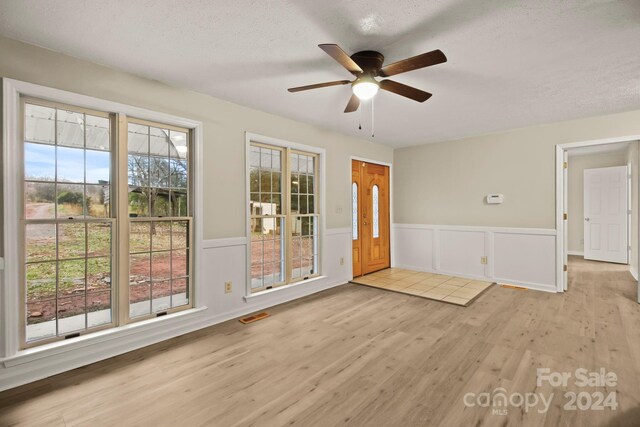 unfurnished room with ceiling fan, plenty of natural light, a textured ceiling, and light wood-type flooring