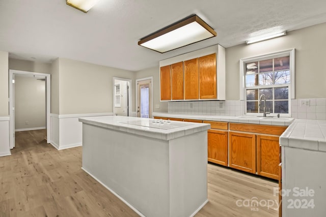 kitchen with tile counters, a center island, light hardwood / wood-style floors, and sink