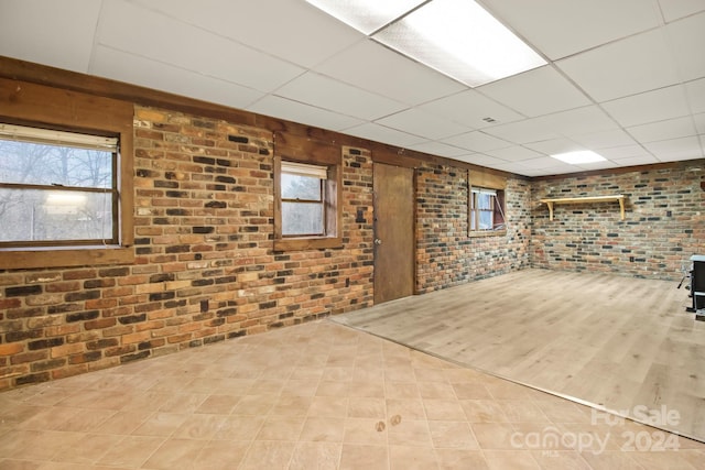 basement featuring a paneled ceiling, a healthy amount of sunlight, and brick wall